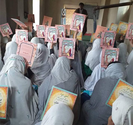 Afghan girls holding up copies of The Old Woman and the Eagle in a classroom