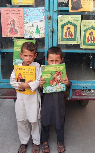 2 Afghan children with Hoopoe books in front of Moska Mobile Library