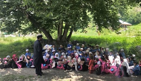 Reading Hoopoe books to children seated under a tree in Afghanistan