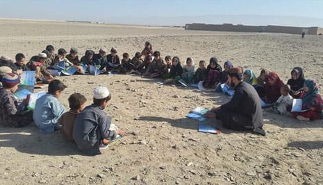 Kids reading in a large circle amidst an arid landscape in Afghanistan