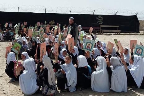 Afghan girls seated outside holding up copies of Hoopoe books