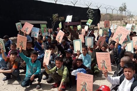 Afghan boys near barbed wire fence holding up copies of Hoopoe books