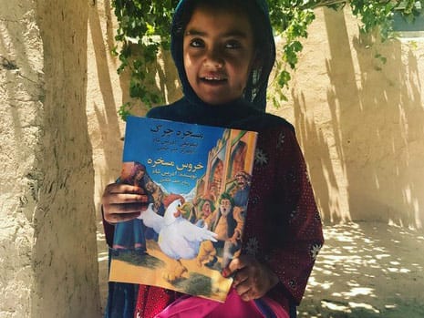 Afghan girl seated in the shade holding a copy of The Silly Chicken