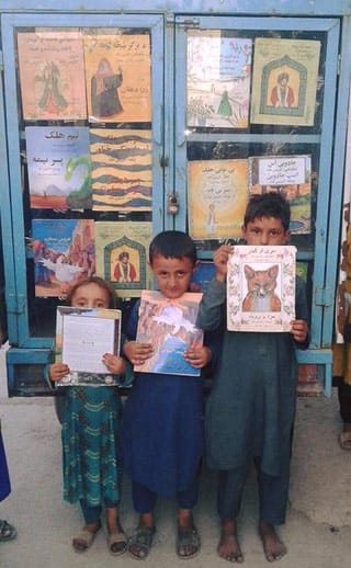 3 Afghan children with Hoopoe books in front of the Moska Mobile Library