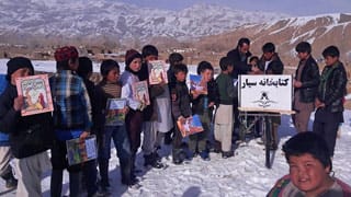 Afghan kids with a variety of Hoopoe books in a snow covered landscape